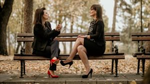 Two Women Sitting On A Bench Speaking Italian To Each Other Learning A New Language
